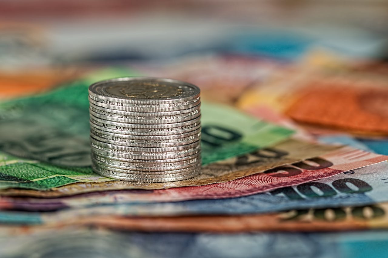 creative-02 A stack of coins on top of various colored banknotes, symbolizing finance and currency.