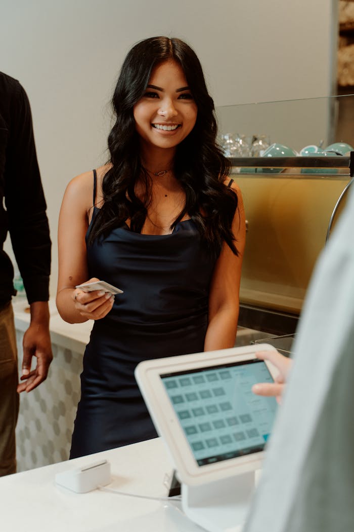 digital A woman in a black dress smiling while making a cashless payment at a store.
