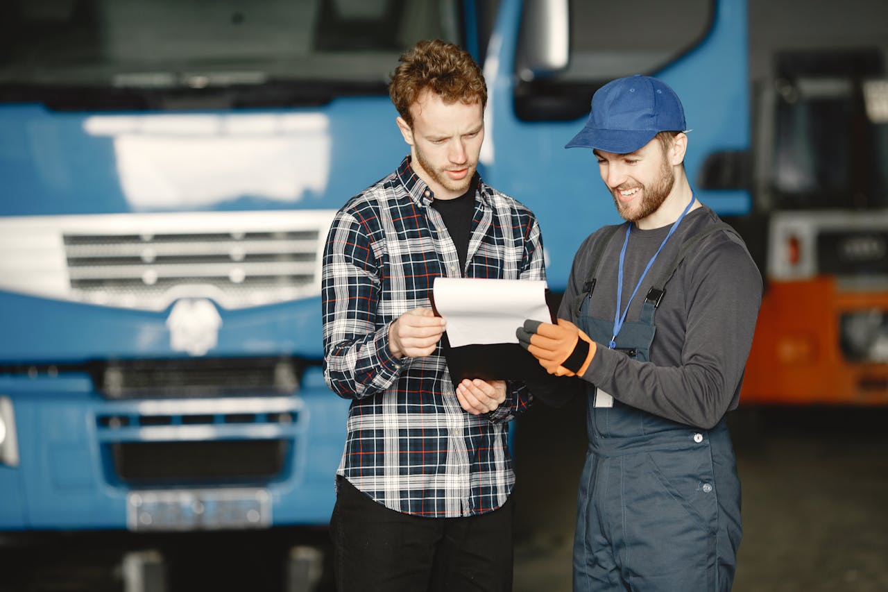 creative Two men in discussion over vehicle maintenance documents in a garage setting with trucks in the background.