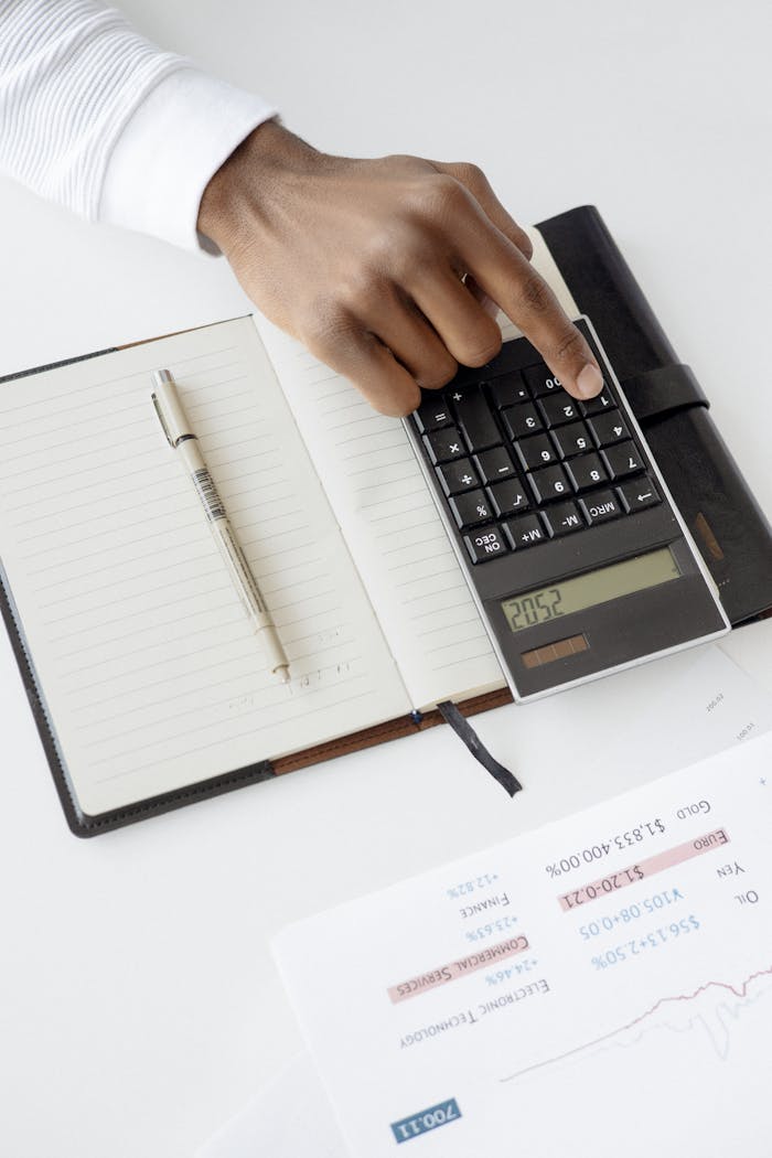 why-choose-us A hand using a calculator with financial documents and notebook, depicting an office setup for financial analysis.